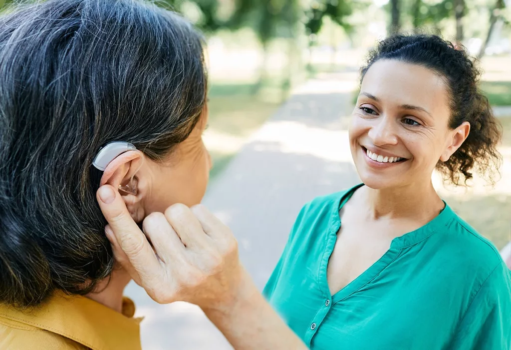 Mature woman with a hearing aid talking face to face with her female friend outdoors. 